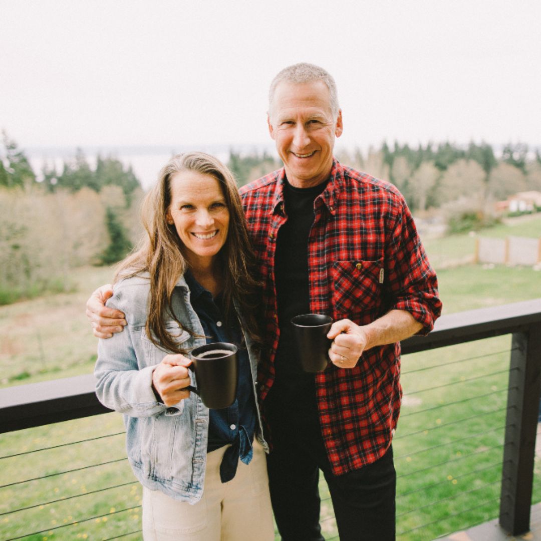 Carol and Eric Blanchet, owners of Talking Crow Coffee Roasters standing on a balcony holding mugs of coffee.