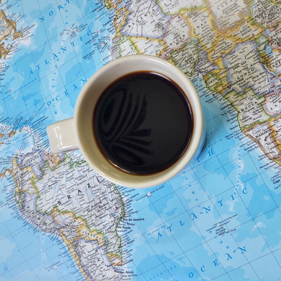 World map with cup of black coffee on top.