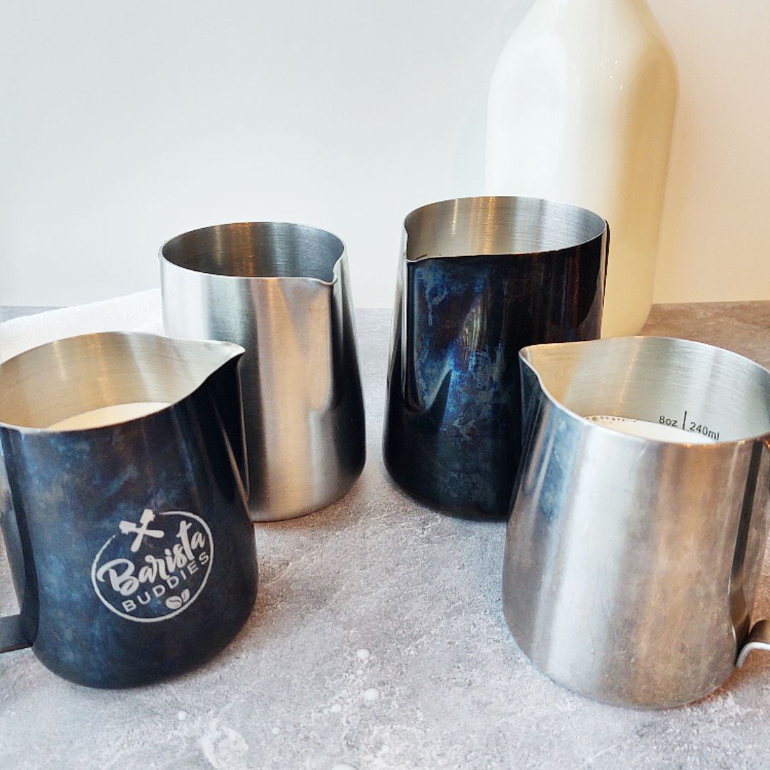 4 latte pitchers filled with milk. Glass milk bottle in the background.