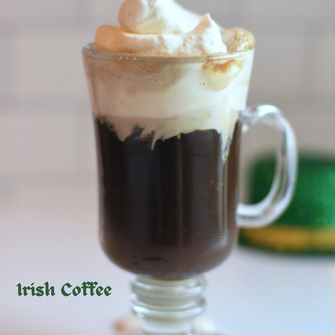 Glass mug of Irish coffee topped with whipped cream and a green leprechaun hat in the background.