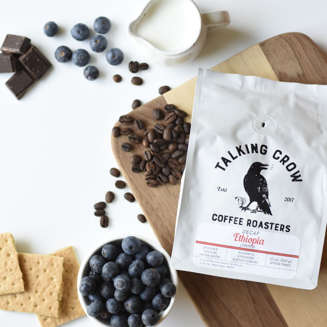 Bag of Talking Crow Coffee Roasters specialty decaf single origin Ethiopian coffee on a wood board with chocolate pieces, graham crackers and blueberries