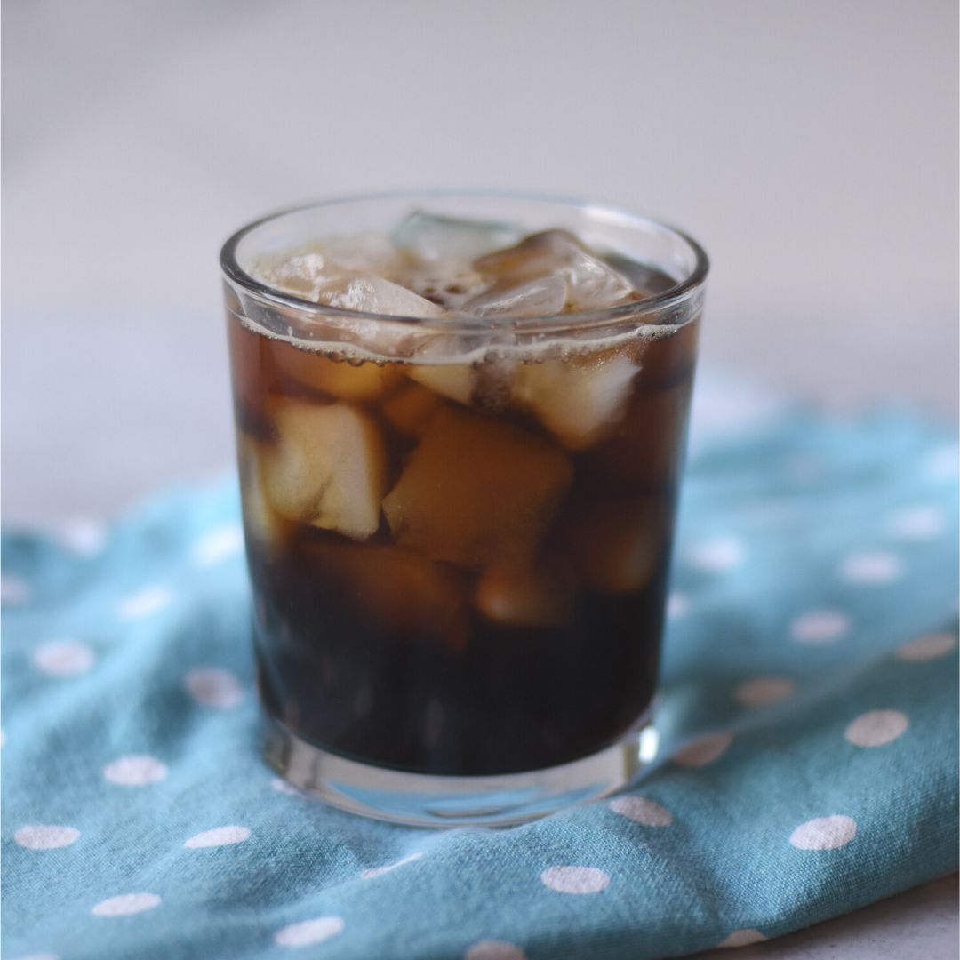 Glass with cold brew coffee over ice on a blue polka dot towel.