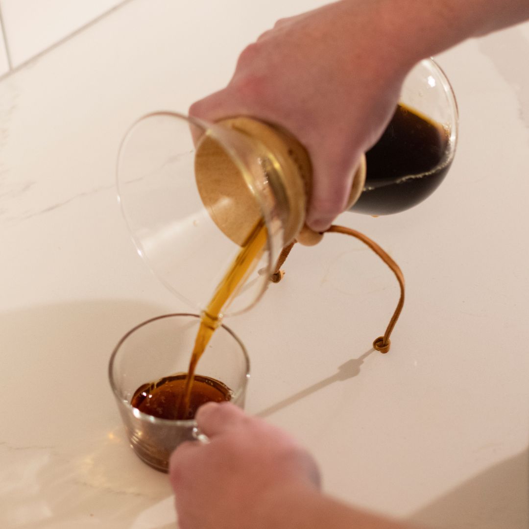 Pouring a cup of coffee from a Chemex brewer into a glass mug
