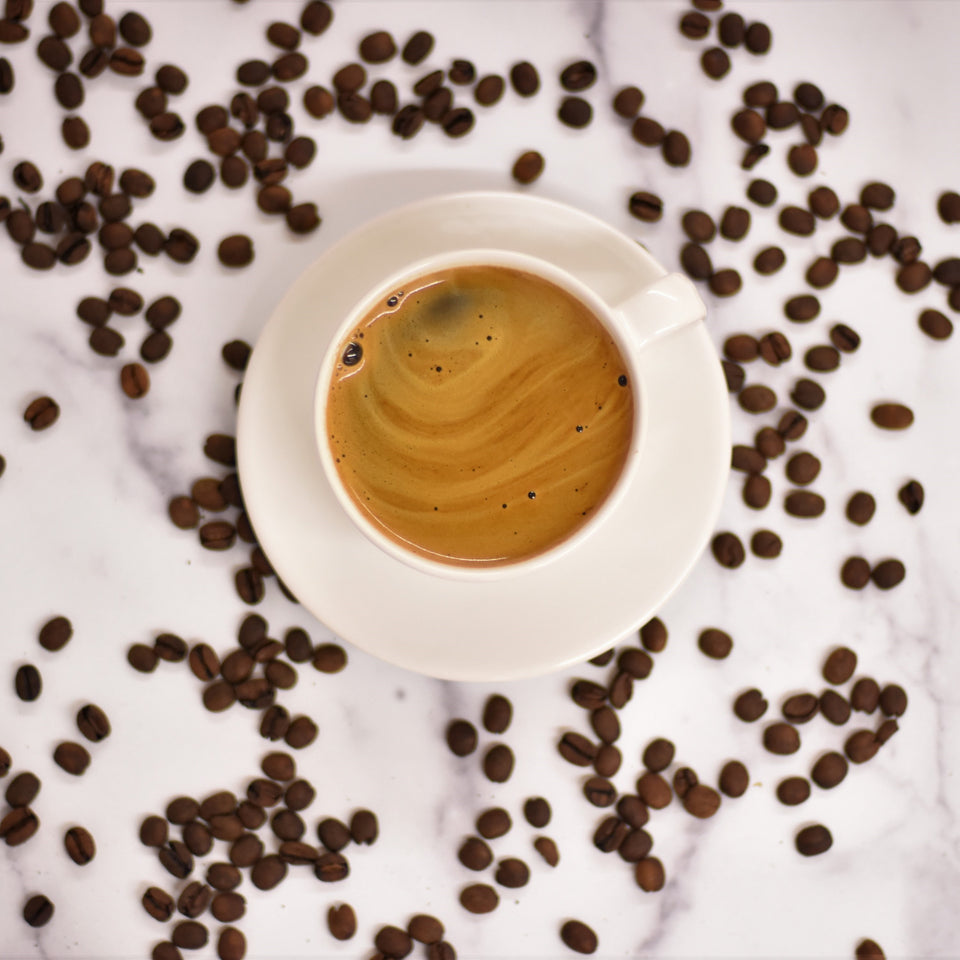 mug of espresso with crema and coffee beans scattered around