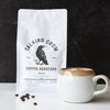 Coffee bag from Talking Crow Coffee Roasters with a mug and decaf coffee beans on a dark background